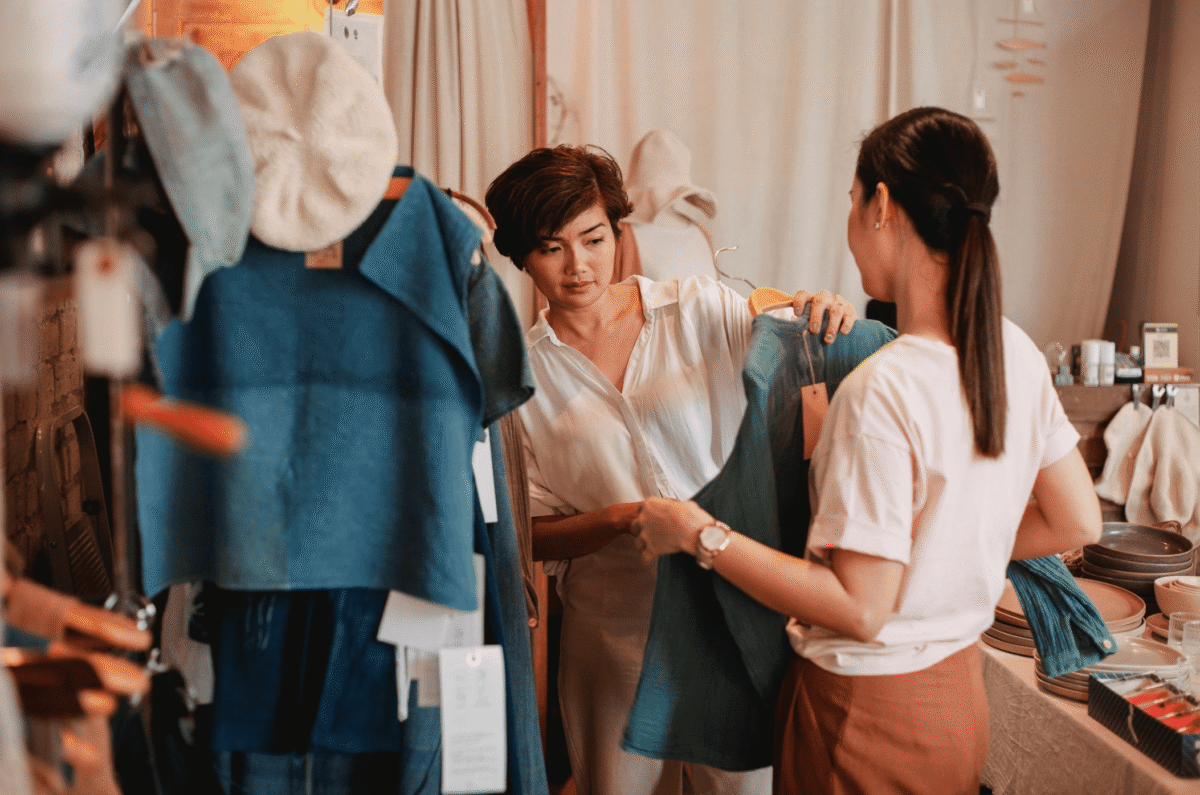 Retail associate helping a customer choose clothing inside a fashion store.