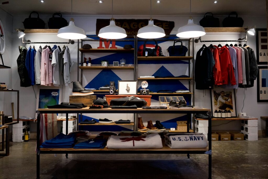 Retail apparel store interior with organized clothing displays, merchandising tables, and wall-mounted product shelving.