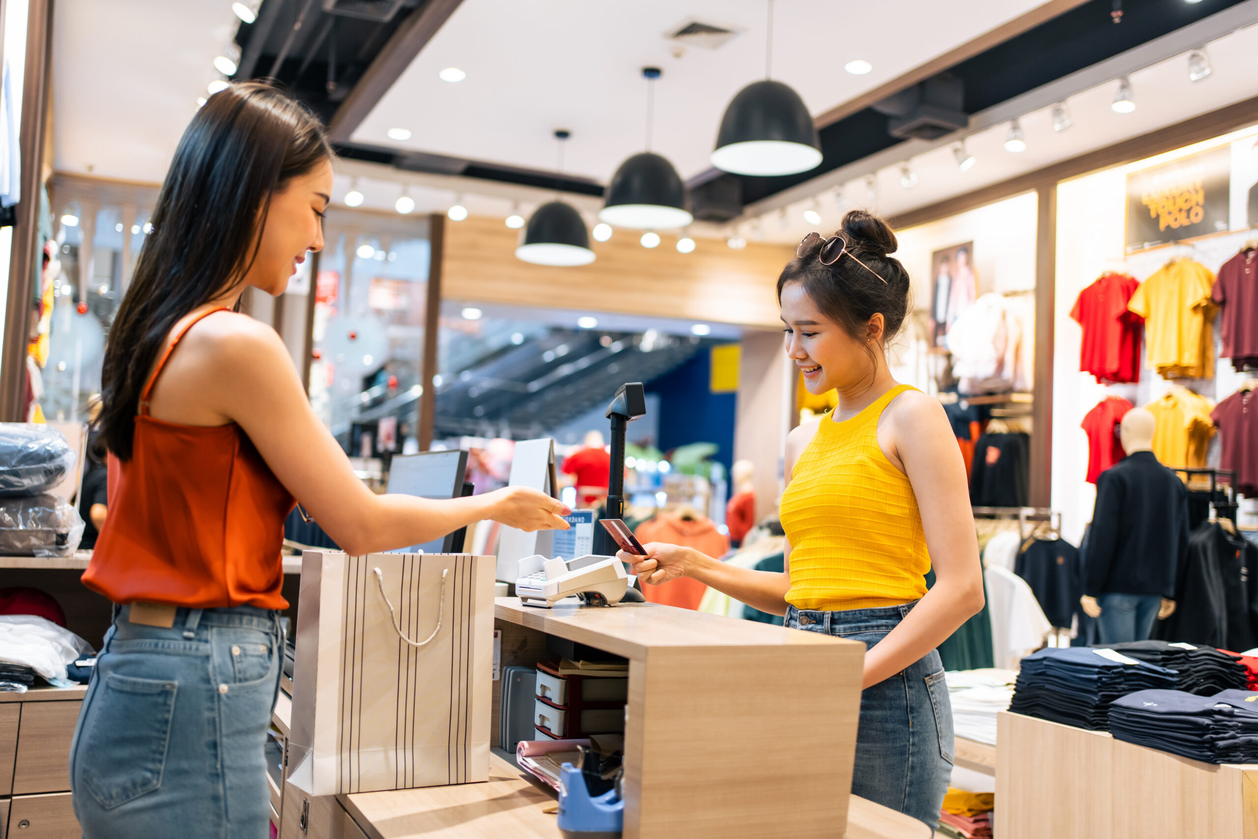 Asian young woman use credit card pay clothes product in shopping mall. Attractive happy girl enjoy walk in department store to choose dress and new t-shirt from clothing racks in marketplace center.