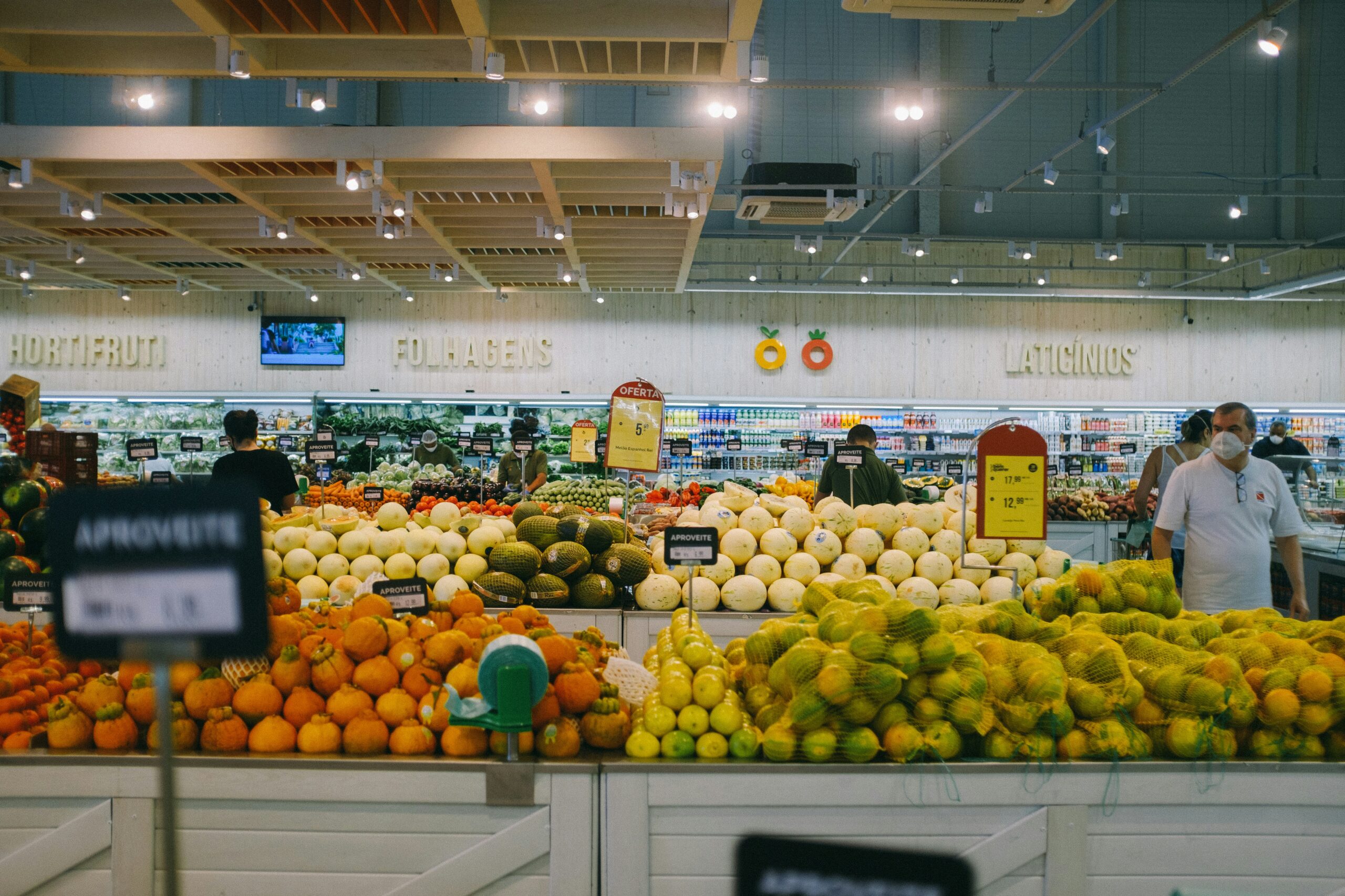 Wide view of a supermarket produce department with bulk displays of melons, oranges and citrus