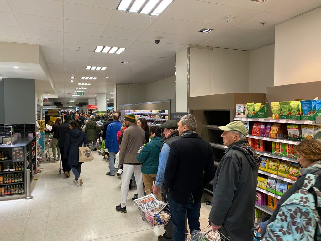Shoppers waiting in line at a supermarket food to go counter during a busy trading period