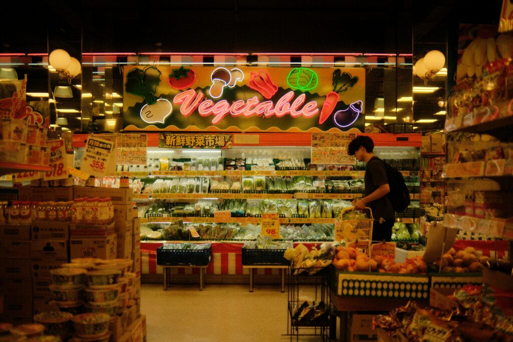 Shopper with a basket choosing vegetables from a chilled produce display.