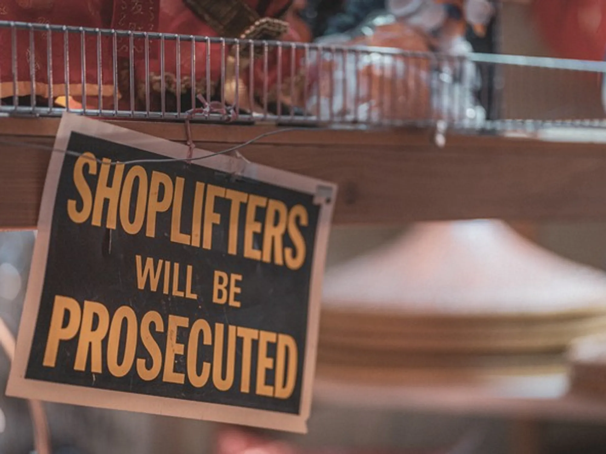 A weathered black and orange sign hanging in a shop reading shoplifters will be prosecuted.