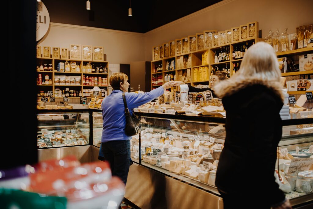 Customer at a deli counter being served cheese by a shop assistant.