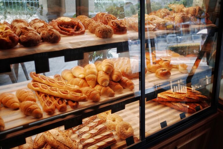 Bakery display case filled with fresh bread and pastries on three lit shelves.